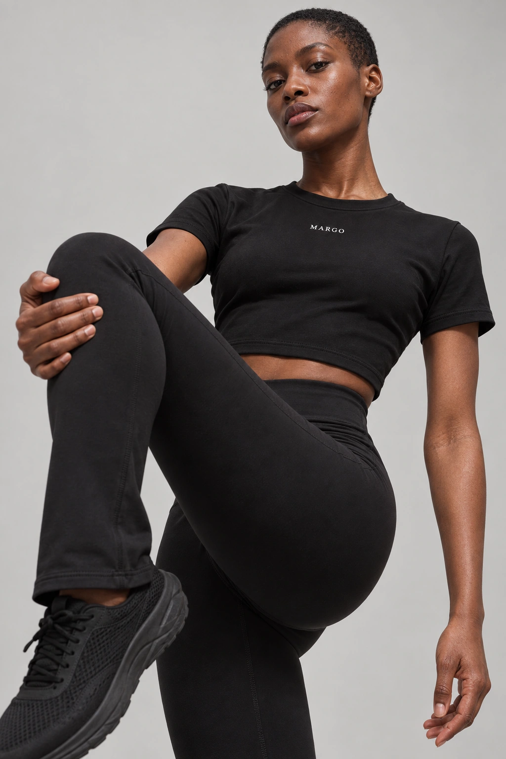 MARGO Sculpt Crop, worn by a woman with a buzz cut in a raised-knee athletic pose in a gray studio